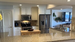 Una cocina moderna con armarios blancos, electrodomésticos de acero inoxidable, encimeras de granito y taburetes de madera.