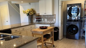 Una cocina con encimeras de granito, armarios blancos, una isla de madera, un refrigerador de acero inoxidable y lavadora y secadora integradas.