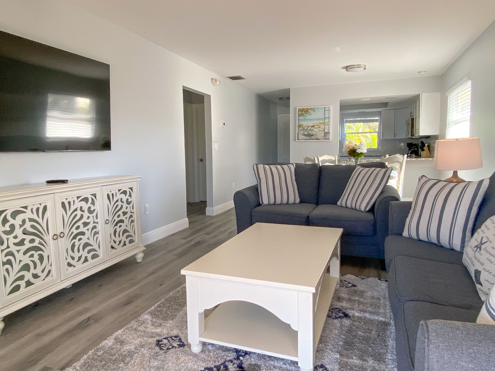 A living room with a sofa, a coffee table, and a TV. There is a kitchen in the background.