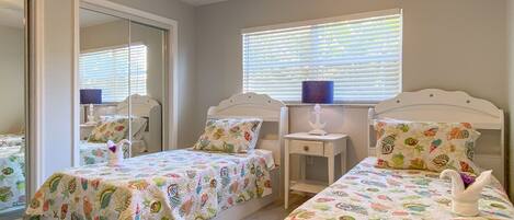 A bedroom with two single beds, a ceiling fan, a window with blinds, and a mirror.
