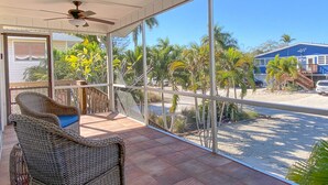 A room with a large glass door leading to a balcony with a wicker chair and a ceiling fan. - Spacious Beach Retreat, Steps to Sugary Sand, Conveniences and Fun! (Fort Myers Beach)