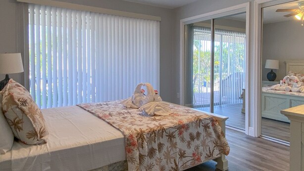 A bedroom with a bed, a ceiling fan, and a view of the outside through a sliding glass door. - Spacious Beach Retreat, Steps to Sugary Sand, Conveniences and Fun! (Fort Myers Beach)