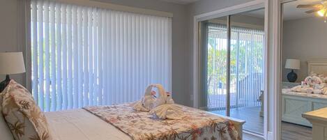 A bedroom with a bed, a ceiling fan, and a view of the outside through a sliding glass door.