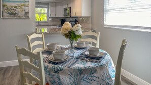 A dining area with a table set for four, white chairs, and a vase with flowers. - Spacious Beach Retreat, Steps to Sugary Sand, Conveniences and Fun! (Fort Myers Beach)