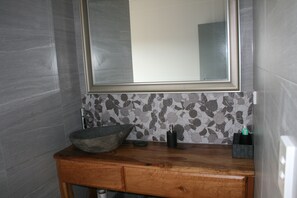 Bathroom features a large mirror, a vanity with a bowl sink, and a tiled backsplash with a leaf pattern.