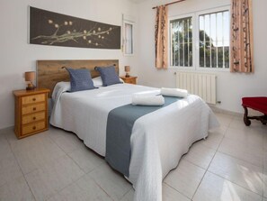 Un dormitorio ordenado con una cama grande, dos mesitas de noche, una ventana con cortinas y un cuadro colgado en la pared.