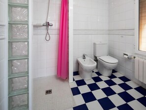 Baño con inodoro blanco, bidé y ducha con cortina rosa. El piso tiene un estampado azul y blanco a cuadros.