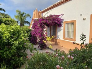 A white building with a terracotta roof, surrounded by lush greenery and purple bougainvillea. - Harmony by Interhome (Jávea)