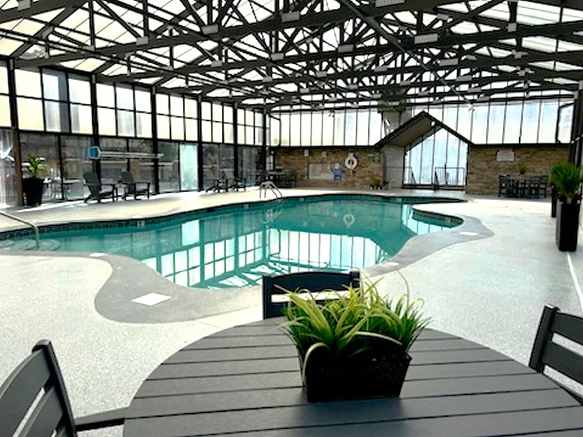 Une piscine intérieure offrant une vue dégagée sur l’espace piscine, un coin salon avec des sièges et une plante en pot posée sur une table.