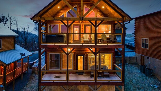 A two-story log cabin with a balcony on the upper floor, surrounded by other cabins. - Near Dollywood! Beautiful Mountain Views, Hot Tub & Resort Indoor Heated Pool (Sevierville)