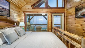 A wooden cabin bedroom with a bed, pillows, a ceiling fan, and a window with blinds. - Near Dollywood! Beautiful Mountain Views, Hot Tub & Resort Indoor Heated Pool (Sevierville)