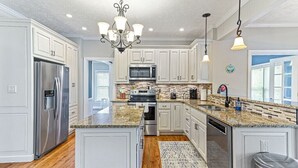 Una cocina amplia con armarios blancos, encimeras de granito y electrodomésticos de acero inoxidable, además de una isla central.