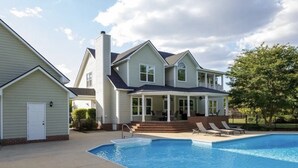 Una casa de dos pisos con piscina, un porche cubierto y chimenea de ladrillo.