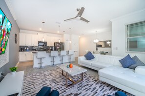 Un salon moderne avec un canapé blanc, une table basse et une cuisine en arrière-plan.