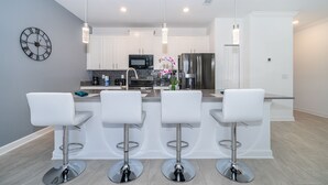 Uma cozinha moderna com banquetas brancas, eletrodomésticos de aço inoxidável e iluminação pendente.