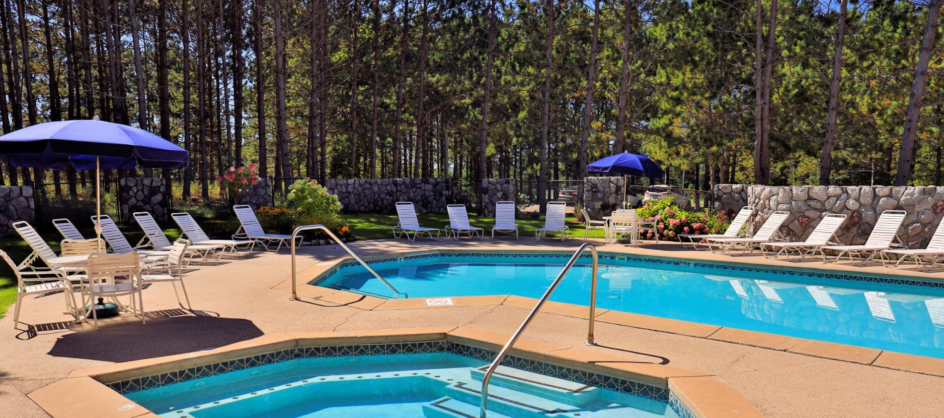 A pool area with lounge chairs and umbrellas, surrounded by a stone wall and trees.