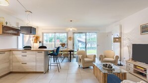 Ein modernes Wohnzimmer mit einer Couch, einem Couchtisch und einem Fernseher. Es gibt eine Küchenzeile mit Schränken sowie einen Esstisch mit Stühlen.
