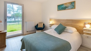Ein Schlafzimmer mit Bett, Nachttisch, Sessel, Gemälde und Blick ins Freie.