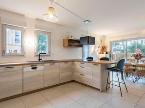 Une cuisine moderne dotée d’un grand îlot central, d’appareils électroménagers intégrés et d’un coin repas avec espace extérieur aménagé.