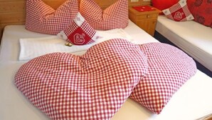 Uma cama com almofadas xadrez vermelhas e brancas, uma cabeceira de madeira e uma mesinha de cabeceira com almofada xadrez vermelha e branca.