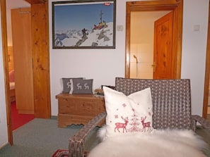 A cozy room with a wooden dresser, a framed picture on the wall, and a chair with a fur throw.