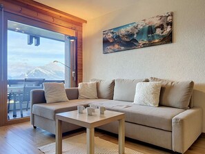 A modern living room with a sofa, a coffee table, and a painting of mountains.