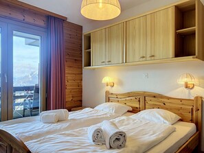 A hotel room with a bed, wooden headboard, built-in wooden cabinets, and a view of mountains through a large window.