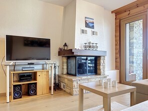 Un salon doté d’un téléviseur à écran plat, d’une cheminée, d’un meuble de rangement en bois et d’un mur en pierre.