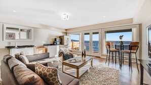 A modern living room with a sofa, coffee table, and a view of the sea through large glass doors. - 10 Mile Point Surfside Suite (Victoria)