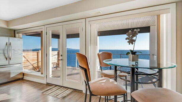 A modern kitchen with a refrigerator, a dining area with a glass table and chairs, and a view of the sea through large sliding glass doors. - 10 Mile Point Surfside Suite (Victoria)