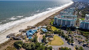 An aerial view of a coastal hotel with multiple buildings, a beach, and a parking area.