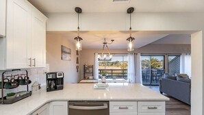 A modern kitchen with white cabinetry, a central island, pendant lighting, and a view to a balcony.