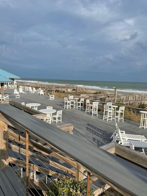 A beachside patio with white chairs and tables, overlooking the ocean.