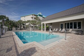 A swimming pool with lounge chairs and a covered seating area, surrounded by a brick patio and palm trees.