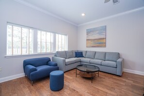 A living room with a sectional sofa, a round coffee table, and a blue ottoman.