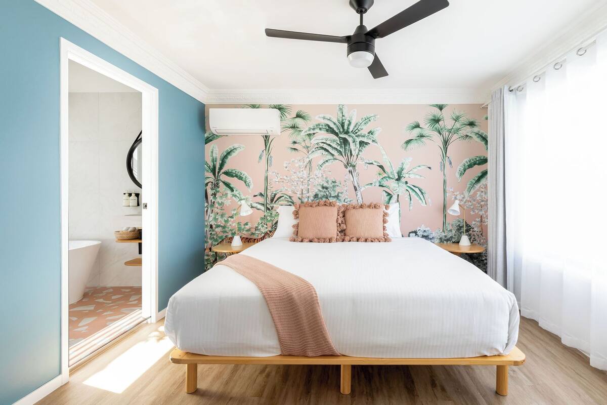 A bedroom with a bed, a ceiling fan, a wall-mounted air conditioner, and a window with curtains.