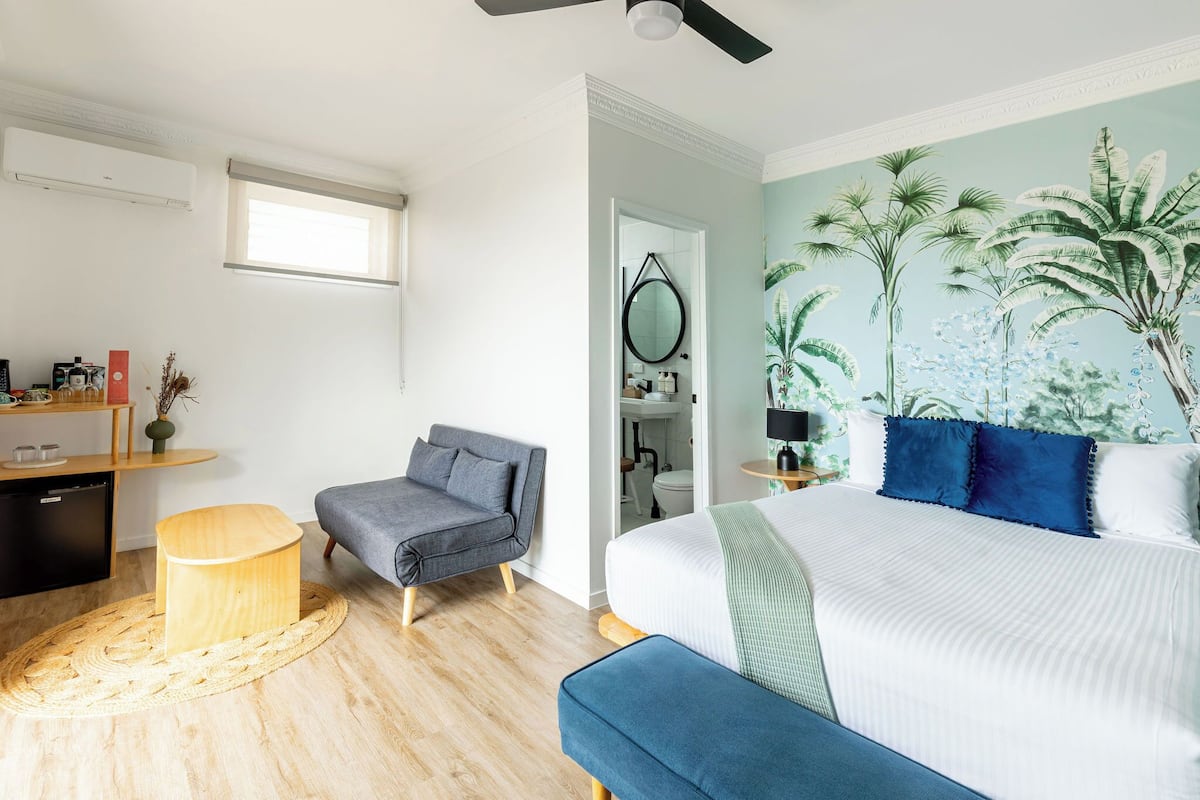 A bedroom with a bed, a chair, a small table, a wardrobe, and a window.