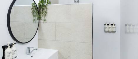 A modern bathroom with a white sink, a round mirror, a handheld showerhead, and a potted plant.