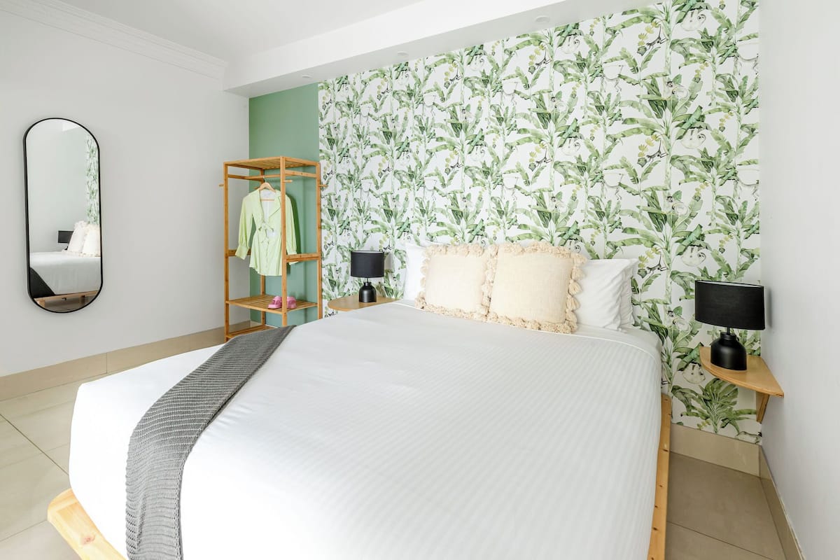 A bedroom with a large bed, a wardrobe, a mirror, and a wall with a leafy pattern.