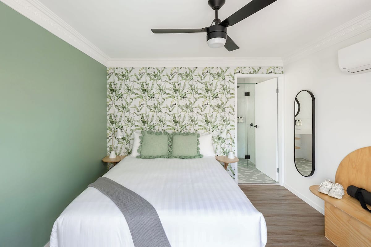 A bedroom with a bed, a ceiling fan, a mirror, and a wooden bench.