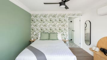Un dormitorio con cama, ventilador de techo, espejo y banco de madera.