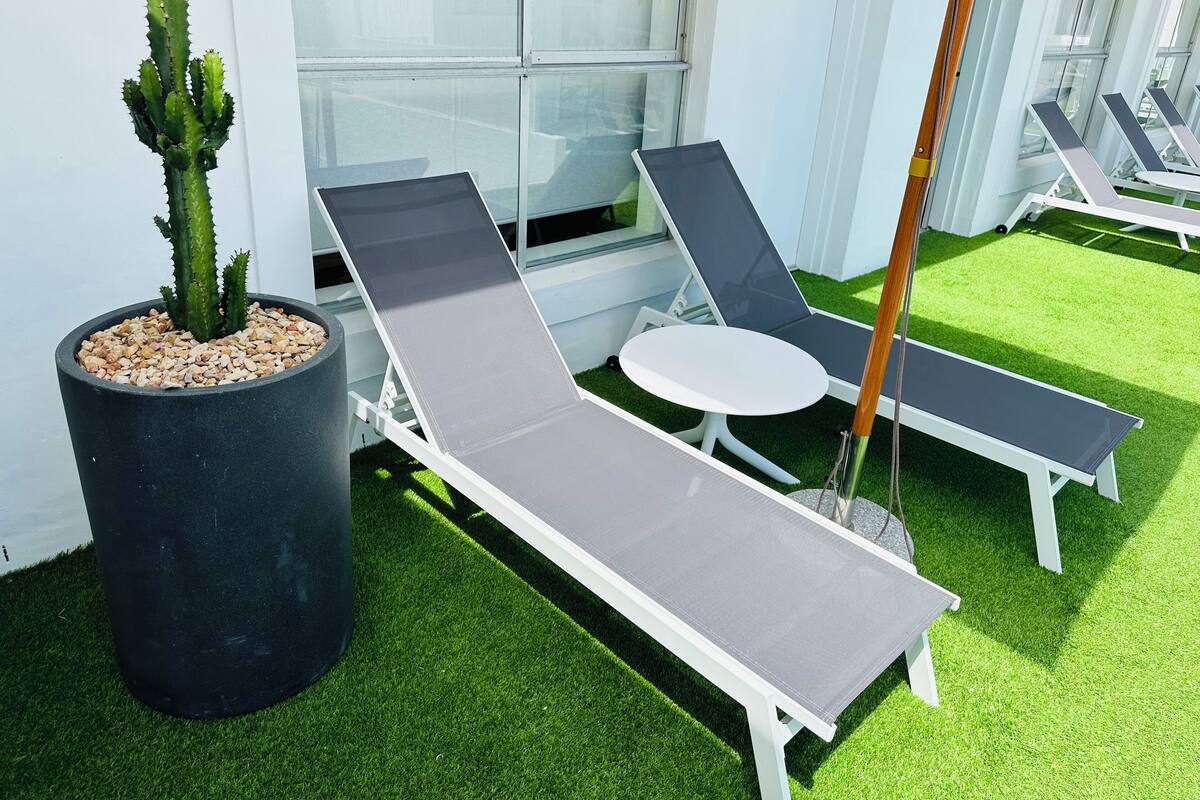 A modern outdoor lounge area with a cactus in a black pot, two grey lounge chairs, and a small white table.