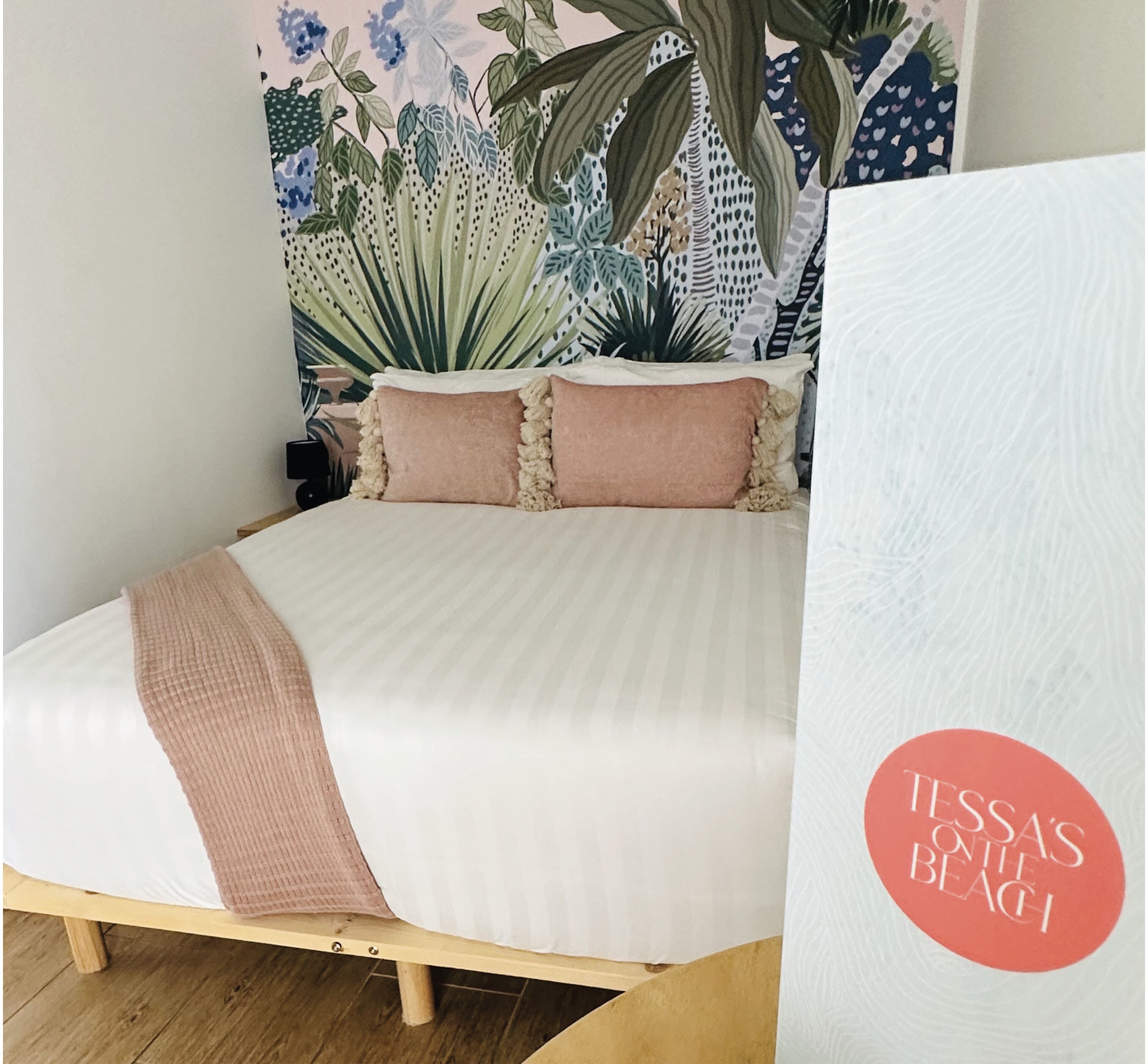 A bed with a white and pink bedding, a wooden frame, and a floral wallpaper backdrop.