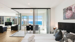 Een moderne hotelkamer met een groot bed, een televisie, een balkon met uitzicht op zee en een zithoek met stoelen en een tafel.