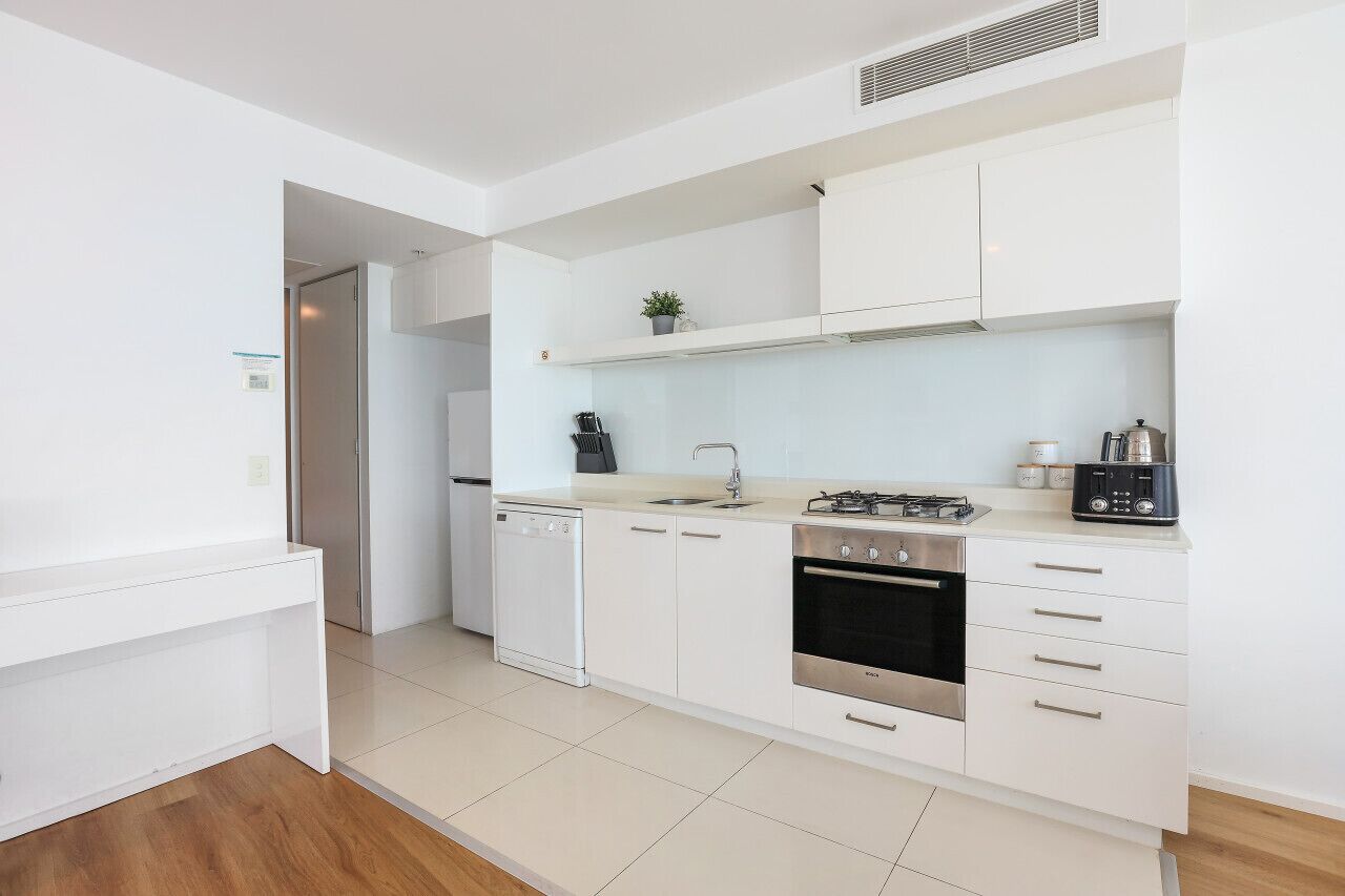 Una cocina moderna con armarios blancos, lavavajillas, estufa y pileta.