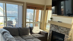 Un amplio sofá modular con chimenea, un televisor de pantalla plana y grandes ventanales que ofrecen vistas al exterior.