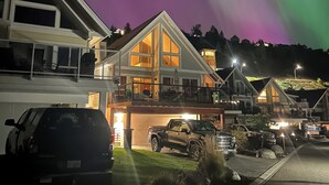 Zona residencial con casas que tienen ventanas amplias y balcones, bajo un cielo nocturno con auroras boreales visibles.