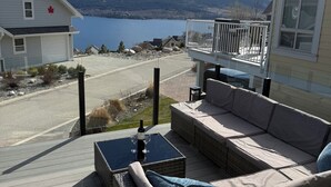 Una terraza con mobiliario de mimbre, una mesa con copas de vino y vistas a un lago y montañas.