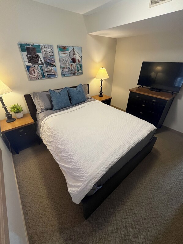 Un dormitorio ordenado con cama, mesitas de noche, lámpara, televisor y decoración en la pared.
