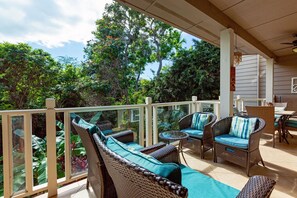 Relax in a serene outdoor space surrounded by lush greenery and trees, with comfortable wicker furniture and a ceiling fan.